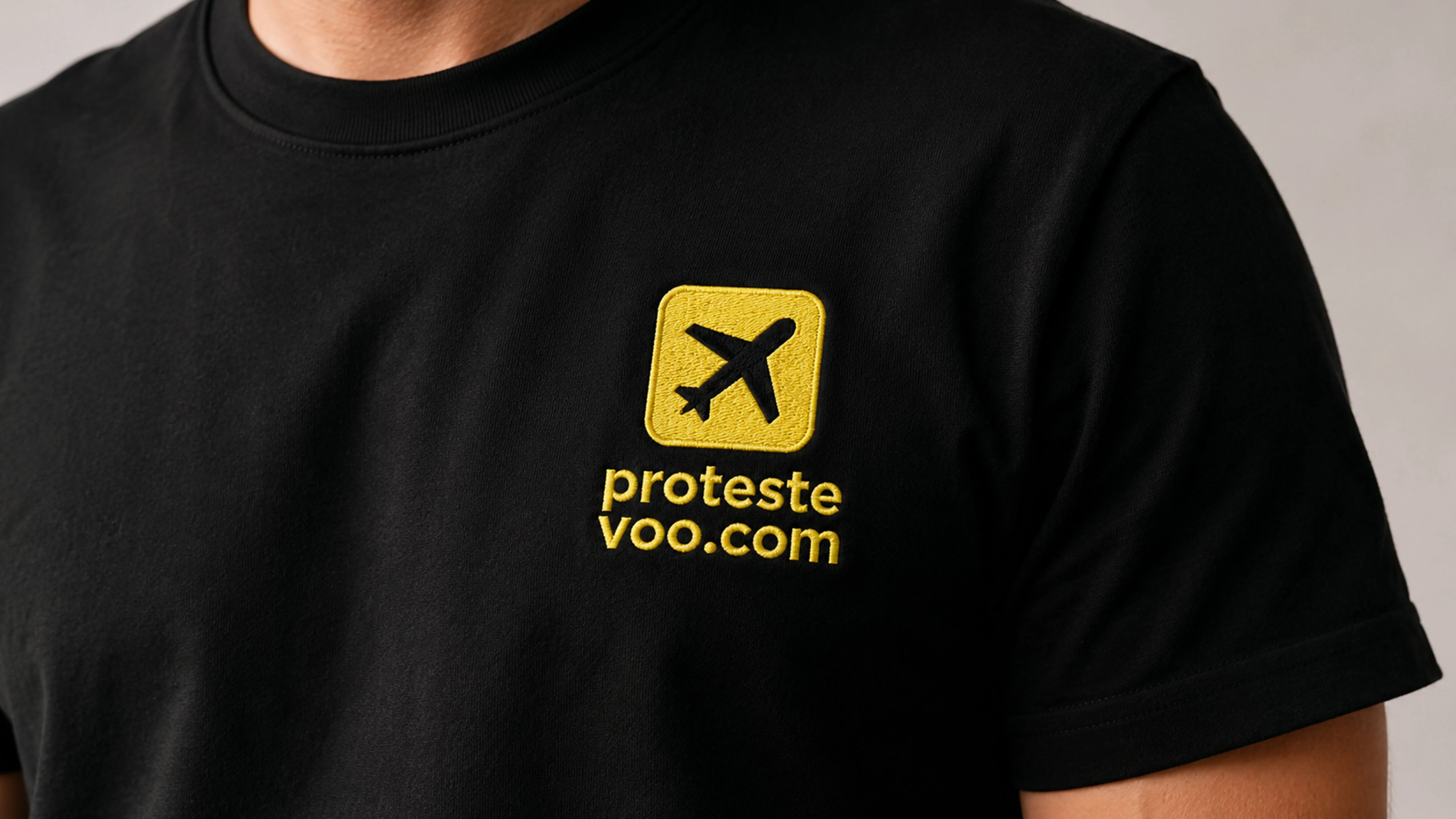 Close-up do logotipo bordado da ProtesteVoo.com em uma camiseta preta.